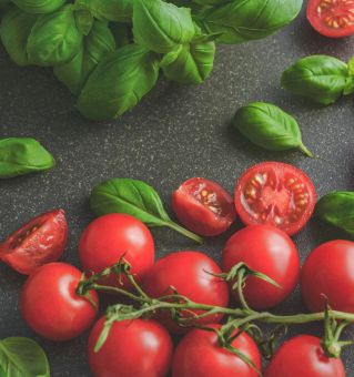 Organic basil leaves with ripe tomatoes on a rustic countertop, highlighting fresh ingredients for cooking.