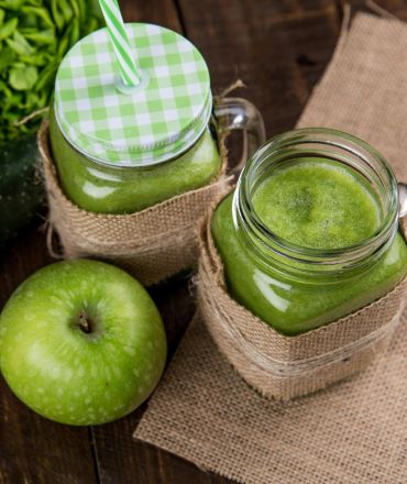 Refreshing green smoothie made with apple, cucumber, and lettuce served in mason jars on wooden background.