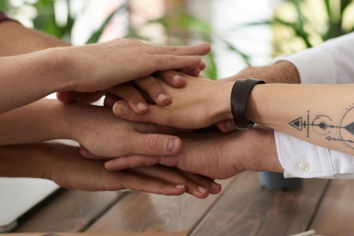 Hands from a diverse team stack on a table symbolizing unity and teamwork in a modern office setting.