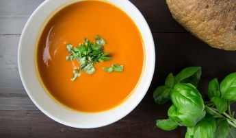 Delicious homemade tomato soup served with basil leaves and rustic bread.