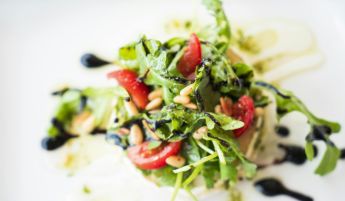 A vibrant arugula salad with cherry tomatoes, pine nuts, and balsamic glaze.