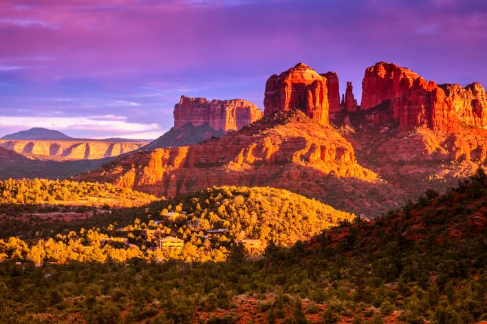 Six women in colorful activewear stretch together on a sunny beach.