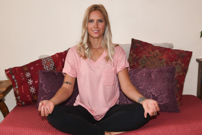 Six women in colorful activewear stretch together on a sunny beach.